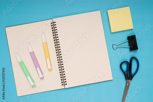 Notebook, scissors, colored pencils, note paper and clamp. back to school. Isolated blue background