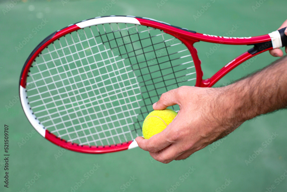 In the men's hand is a tennis racket and a ball against the background of a tennis court.