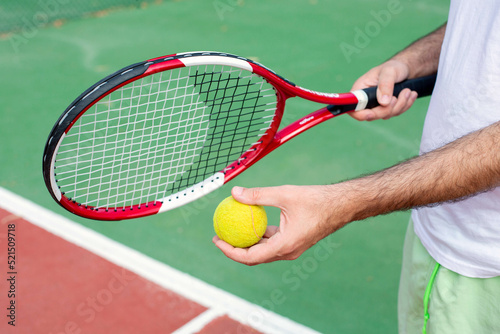 A man in one hand holds a racket and the ball in the other hand stands on a tennis court. The theme of sports and a healthy lifestyle.