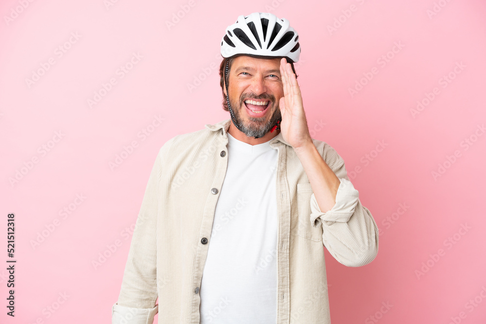 Senior dutch man with bike helmet isolated on pink background shouting with mouth wide open
