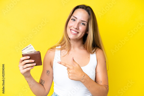 Young caucasian woman holding a wallet isolated on yellow background and pointing it