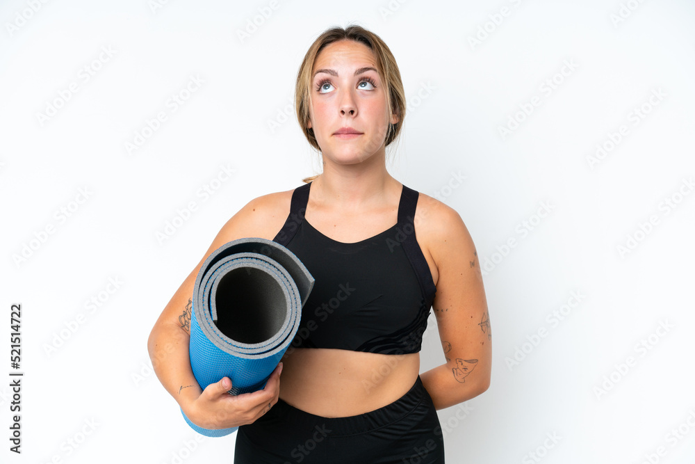 Young caucasian woman going to yoga classes while holding a mat isolated on white background and looking up Young caucasian woman going to yoga classes while holding a mat isolated on white background and looking up