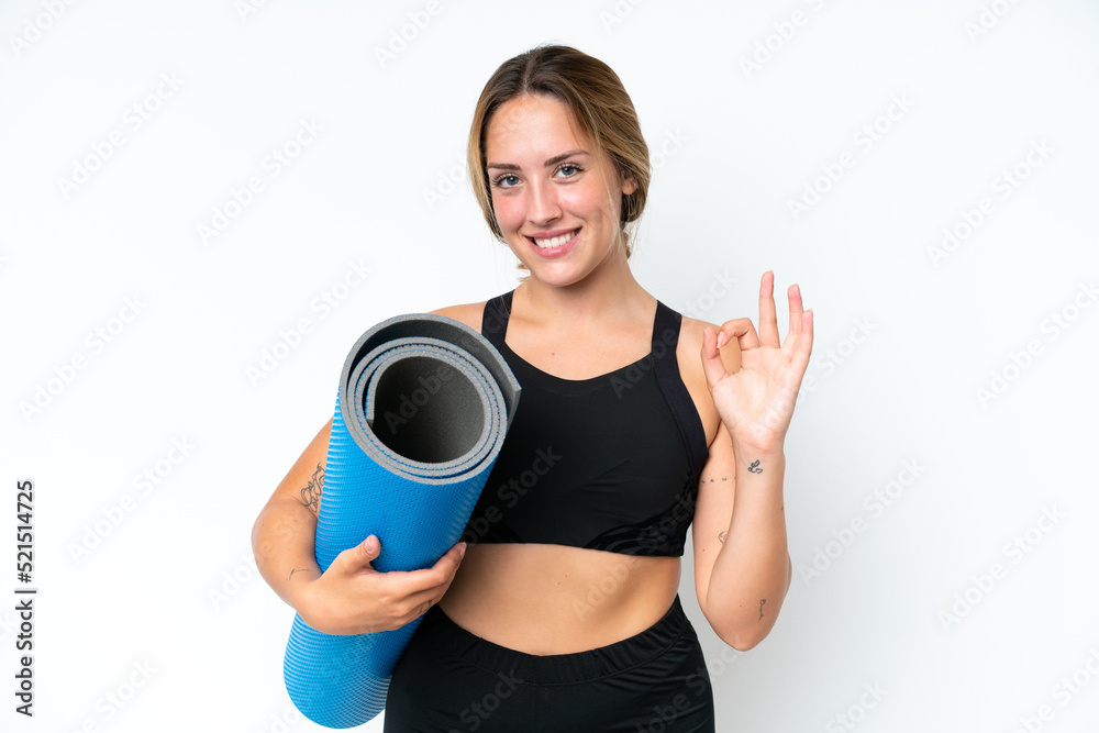 Young caucasian woman going to yoga classes while holding a mat isolated on white background showing ok sign with fingers Young caucasian woman going to yoga classes while holding a mat isolated on white background showing ok sign with fingers