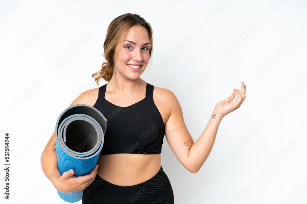 Young caucasian woman going to yoga classes while holding a mat isolated on white background extending hands to the side for inviting to come Young caucasian woman going to yoga classes while holding a mat isolated on white background extending hands to the side for inviting to come