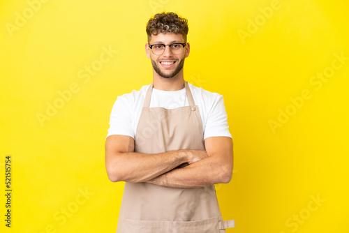 Restaurant waiter blonde man isolated on yellow background keeping the arms crossed in frontal position