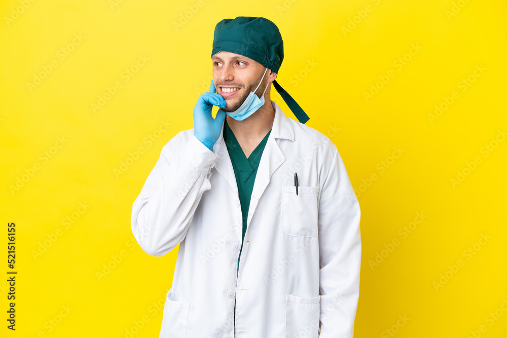Surgeon blonde man in green uniform isolated on yellow background thinking an idea while looking up Surgeon blonde man in green uniform isolated on yellow background thinking an idea while looking up
