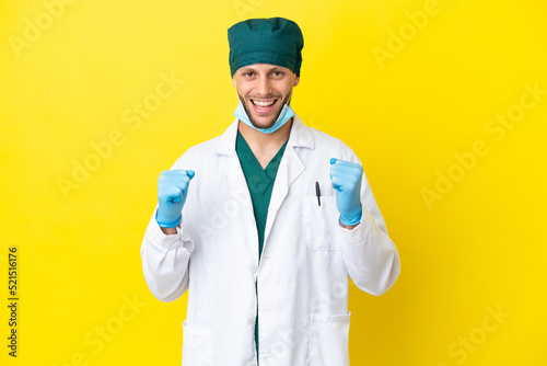 Surgeon blonde man in green uniform isolated on yellow background celebrating a victory in winner position