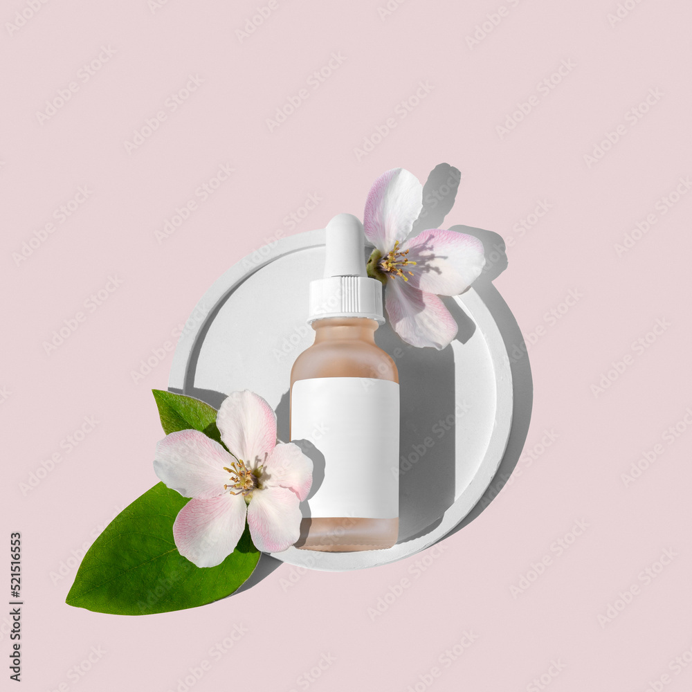 A glass dropper bottle with a pipette on a round flat podium and flowers next to it on a pink background. Organic spa cosmetics. A glass dropper bottle with a pipette on a round flat podium and flowers next to it on a pink background. Organic spa cosmetics.