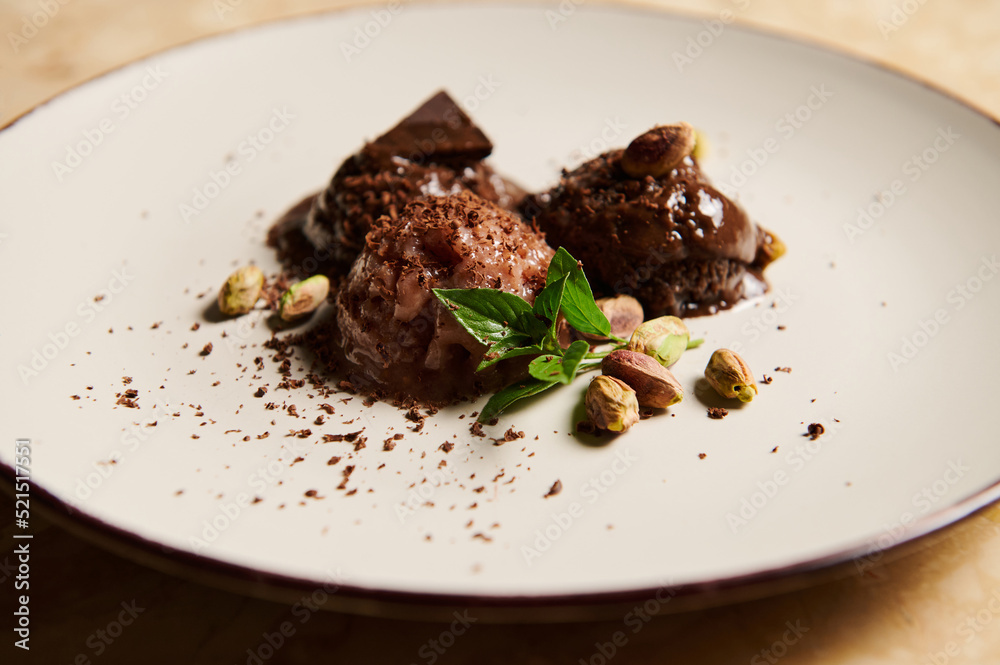 Close-up. Still life. Frozen balls of chocolate ice cream, with pistachio and lemon basil leaves, melting on white plate Close-up. Still life. Frozen balls of chocolate ice cream, with pistachio and lemon basil leaves, melting on white plate