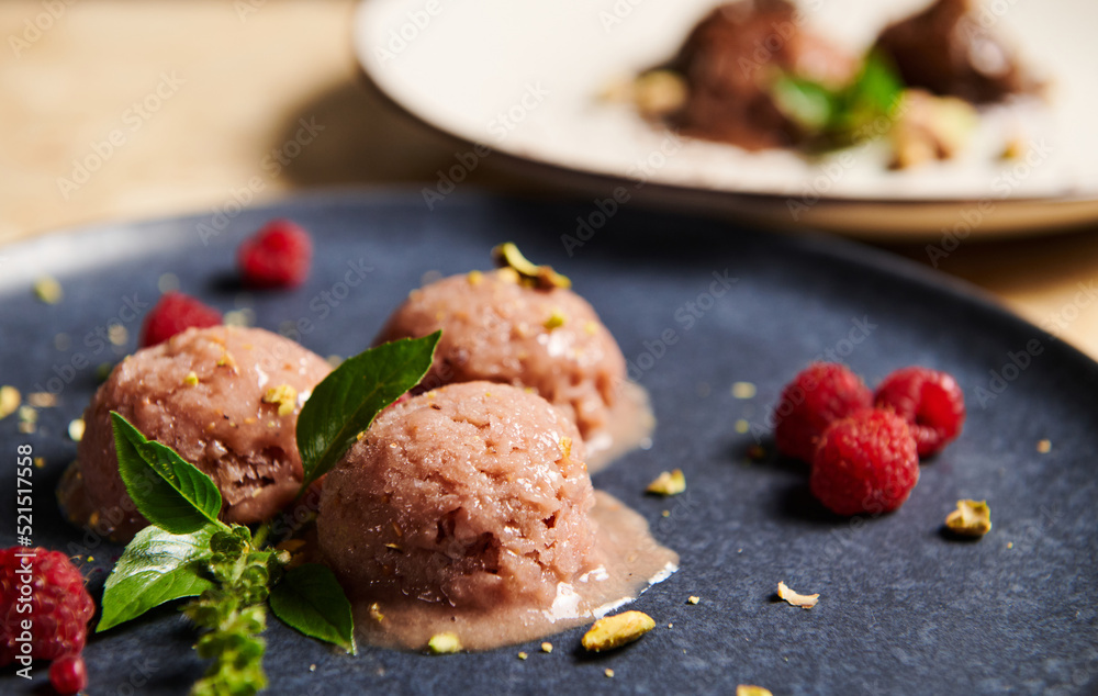 Scoops of raspberry sorbet with sprinkled pistachio, raspberries and lemon basil on dark blue plate. Selective focus Scoops of raspberry sorbet with sprinkled pistachio, raspberries and lemon basil on dark blue plate. Selective focus