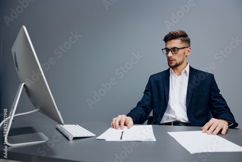 a man in a suit wearing glasses works in front of a computer Gray background