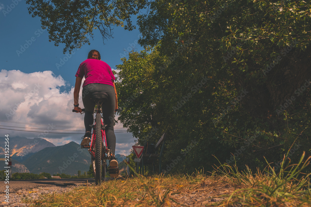 A female cyclist riding the bicycle on a rural road in the French Alps mountains in summer