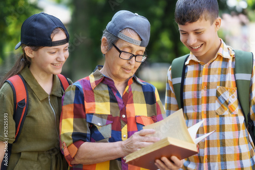 portrait of students and a teacher in a city park, teenage schoolchildren a boy and a girl are standing on the path and discussing lessons with a educator, reading a book and talking