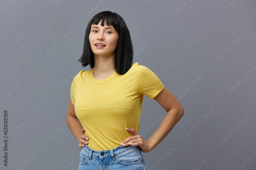 a happy, beautiful, attractive woman stands in a yellow T-shirt and light jeans on a gray background, smiling pleasantly and holding her hands on her belt. Studio Photography a happy, beautiful, attractive woman stands in a yellow T-shirt and light jeans on a gray background, smiling pleasantly and holding her hands on her belt. Studio Photography