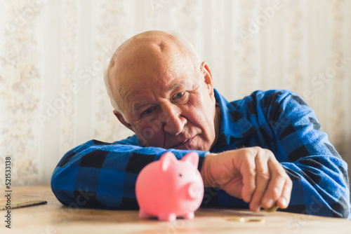 Fotografie Sad, lost and depressed caucasian senior man laying on the table with a piggy bank and counting his last coins
