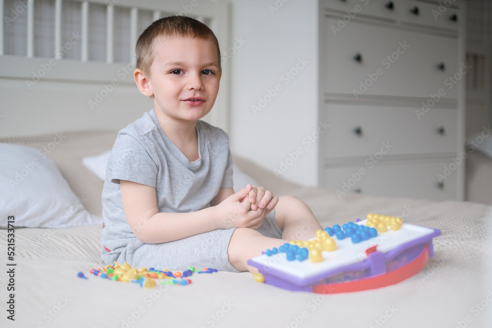 Little happy caucasian boy in a light room on the bed collects color mosaic to creating images Little happy caucasian boy in a light room on the bed collects color mosaic to creating images
