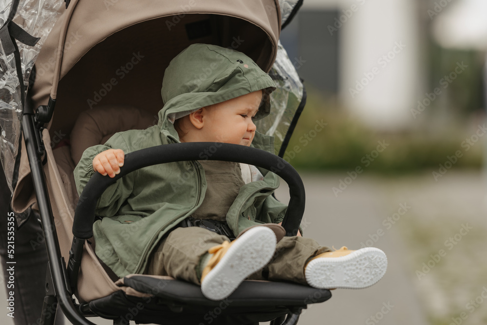 A female toddler is sitting in the stroller on a cloudy day.