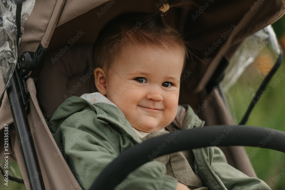 A female toddler is sitting in the stroller on a cloudy day.