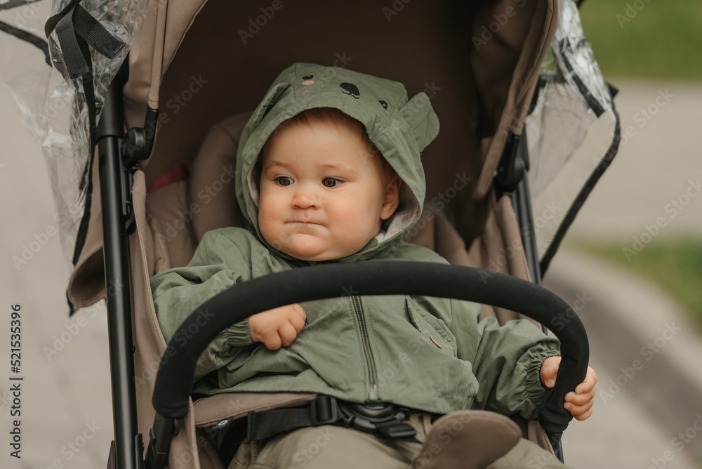 A female toddler is sitting in the stroller on a cloudy day.