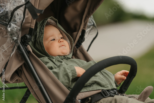 Obraz na płótnie A female toddler is sitting in the stroller on a cloudy day. w salonie