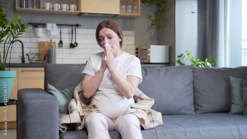 sick pregnant woman with cold cough and temperature blowing nose with runny nose sitting on sofa
