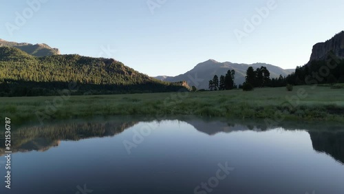 Small pond with mist in the calm pre-dawn glow reflecting the mountains rising up into the sky on the water's surface. Drone shot flying low over water with slow camera tilt up. Filmed in Colorado. photo