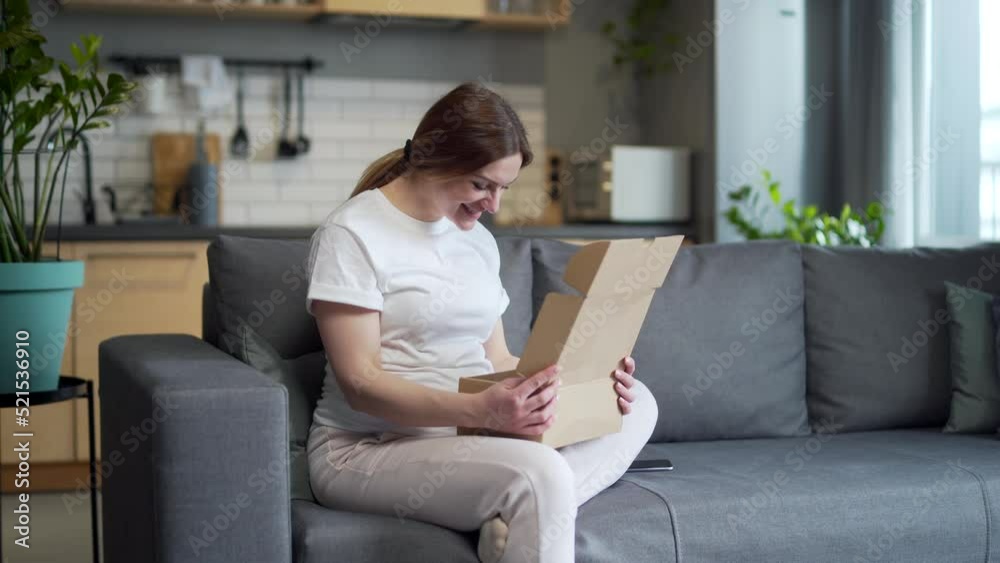 Pregnant beautiful woman received a parcel by courier home, package, gift. He sits on the sofa at home, opens a paper box, rejoices, smiles Pregnant beautiful woman received a parcel by courier home, package, gift. He sits on the sofa at home, opens a paper box, rejoices, smiles