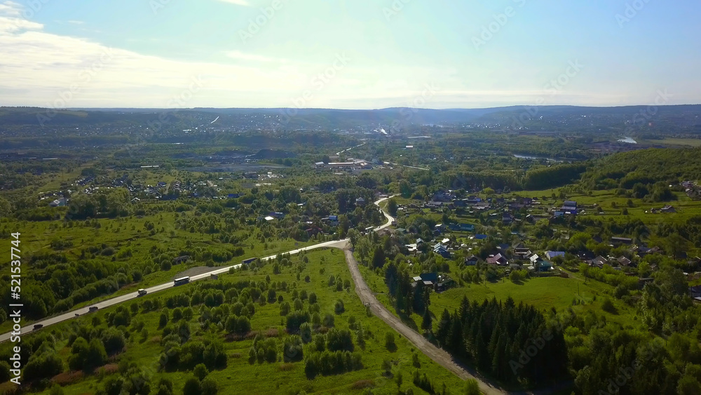 View of the city from a drone. Clip. A summer provincial town with a small road with cars, with low houses, green sunny trees around and a bright blue sunny sky.