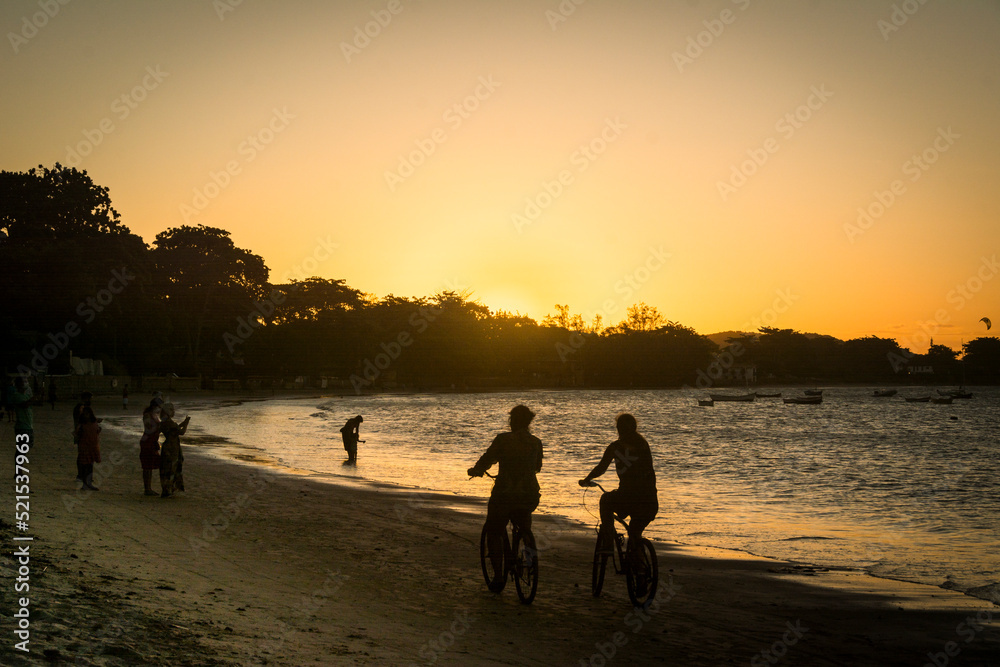 Sunset on the beach with cyclist couple at Buzios town, State of Rio de Janeiro, Brazil. Taken with Nikon D7100 18-200 lens, at 50mm, 1/1600 f 9.0 ISO 125