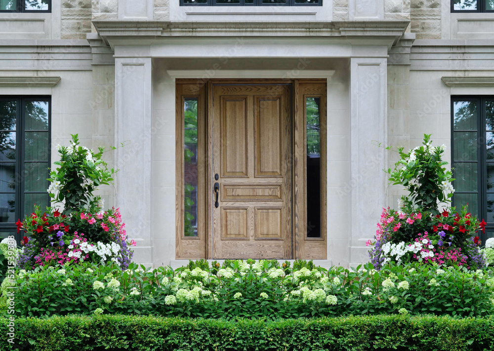 Wood grain front door of house surrounded by columns and summer flowers Wood grain front door of house surrounded by columns and summer flowers