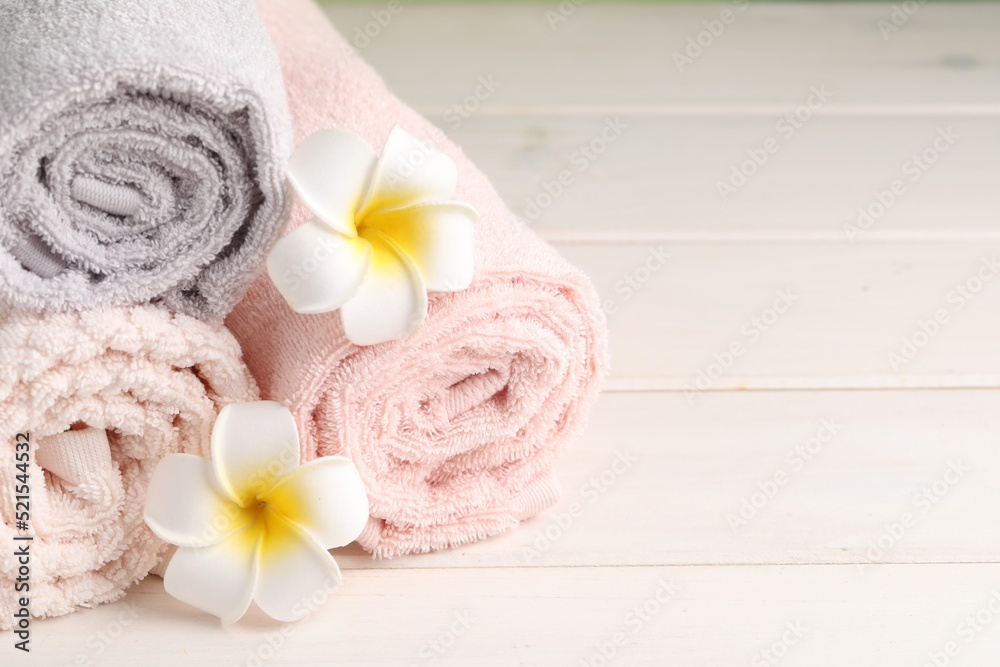 Closeup view of soft folded towels and plumeria flowers on white wooden table, space for text Closeup view of soft folded towels and plumeria flowers on white wooden table, space for text