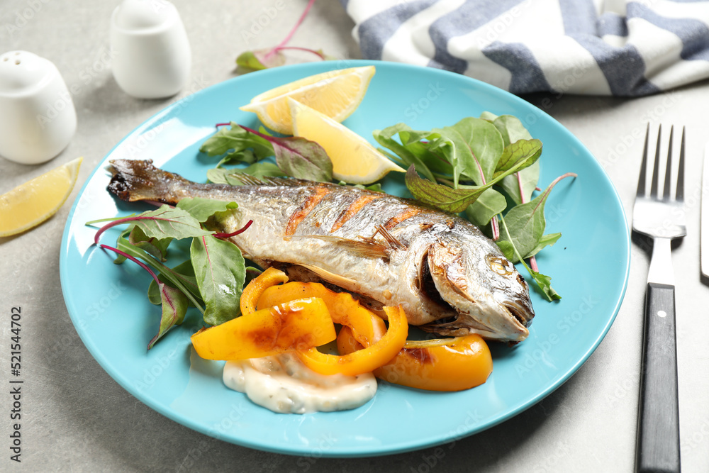 Delicious roasted fish with lemon and vegetables on grey table Delicious roasted fish with lemon and vegetables on grey table
