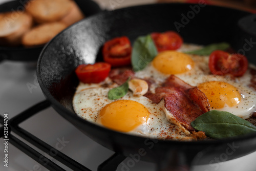 Delicious fried eggs with bacon and tomatoes in pan, closeup