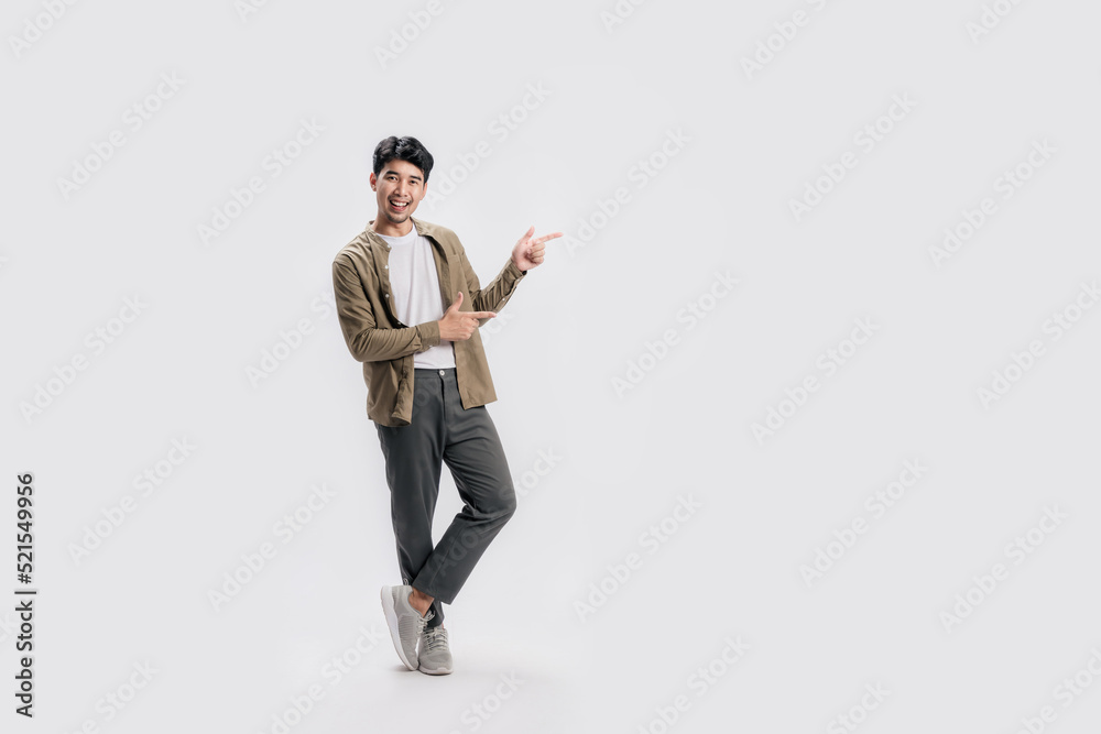 Full length smart young Asian man happy smile standing hand pointing to empty space on white background. Short on studio.