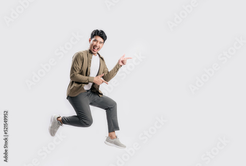 Full length excited handsome young Asian man jumping in air with hand pointing to empty space on white background. Cool man joyful running in copy space. Studio short.
