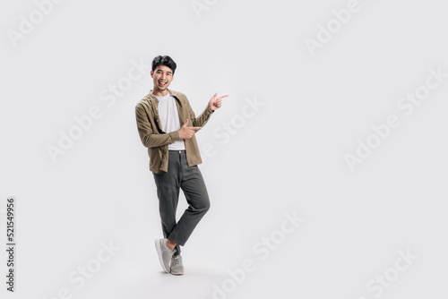 Full length smart young Asian man happy smile standing hand pointing to empty space on white background. Short on studio.