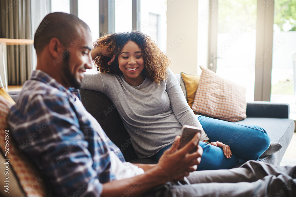 Happy, carefree and relaxed couple reading text on a phone while sitting on a couch. Man and woman smiling and laughing while browsing an online social media app or watching funny videos at home Happy, carefree and relaxed couple reading text on a phone while sitting on a couch. Man and woman smiling and laughing while browsing an online social media app or watching funny videos at home