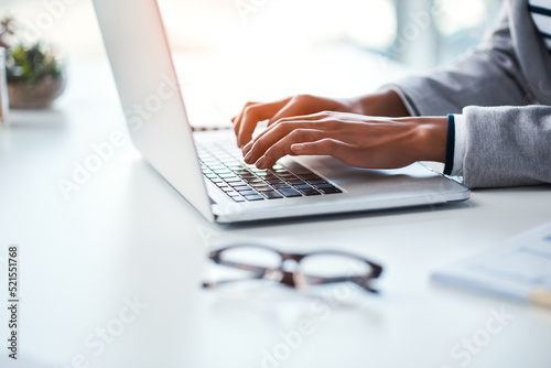 Closeup of hands of a business person typing on a laptop, browsing the internet online and finishing a proposal while sitting at a table in an office at work. One employee networking on the web photo
