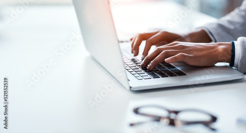 Closeup of hands of a business person typing on a laptop, replying to emails and browsing the internet while sitting at a desk in an office alone at work. Employee searching online and doing research