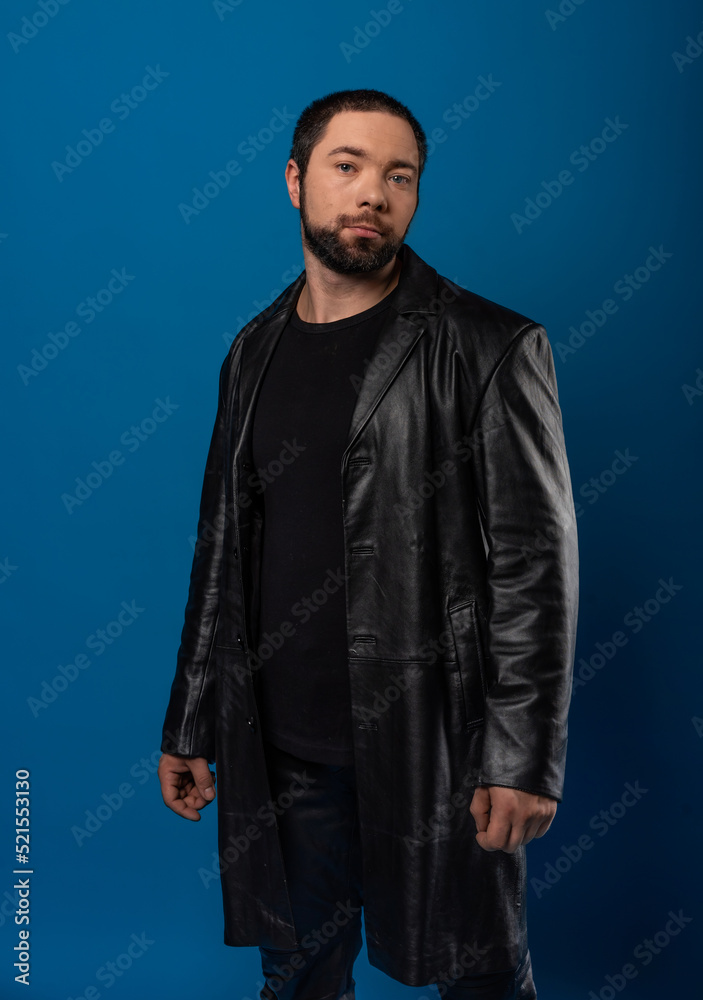 portrait of a man in a studio in a black leather coat. model with a beard on a blue background.