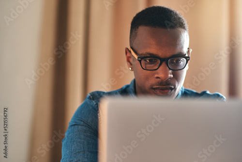 Focused, serious and confident entrepreneur typing on a laptop and reading an email sitting alone in his home office. African american businessman planning and remote working his startup business