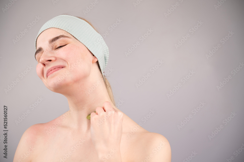 Portrait of a young woman massages her face with a gouache scraper on a white background. Portrait of a young woman massages her face with a gouache scraper on a white background.