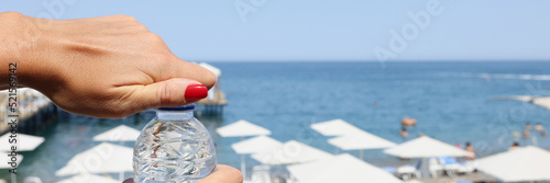 Female hands open a bottle of water on a beach, blurry