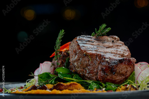grilled meat steak on a black plate with salad and sauce on a dark background macro photo 