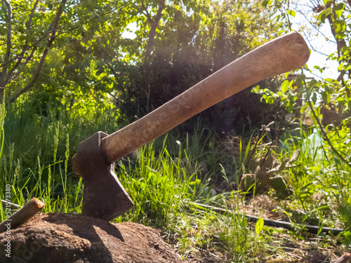 old vintage iron ax sticks out in a stump on a farm on a sunny summer day. Backlight.