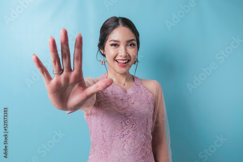 Young Asian woman wearing modern kebaya over blue isolated background doing stop sign with palm of the hand.