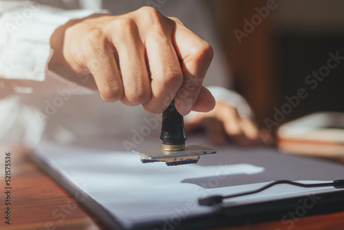 Close up of business hand stamping approved on certificate document in office, Lawyer stamping permit on paperwork at wooden desk. confirmation pass and agreement success.