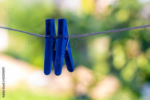 On the clothesline outdoors, there are two clothespins in blue, used as household items for hanging and drying clothes on the day of washing.