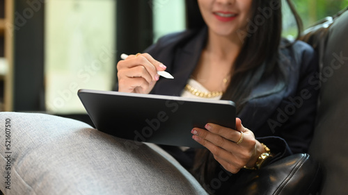 Smiling millennial woman using digital tablet while resting on couch at her personal office. Cropped shot