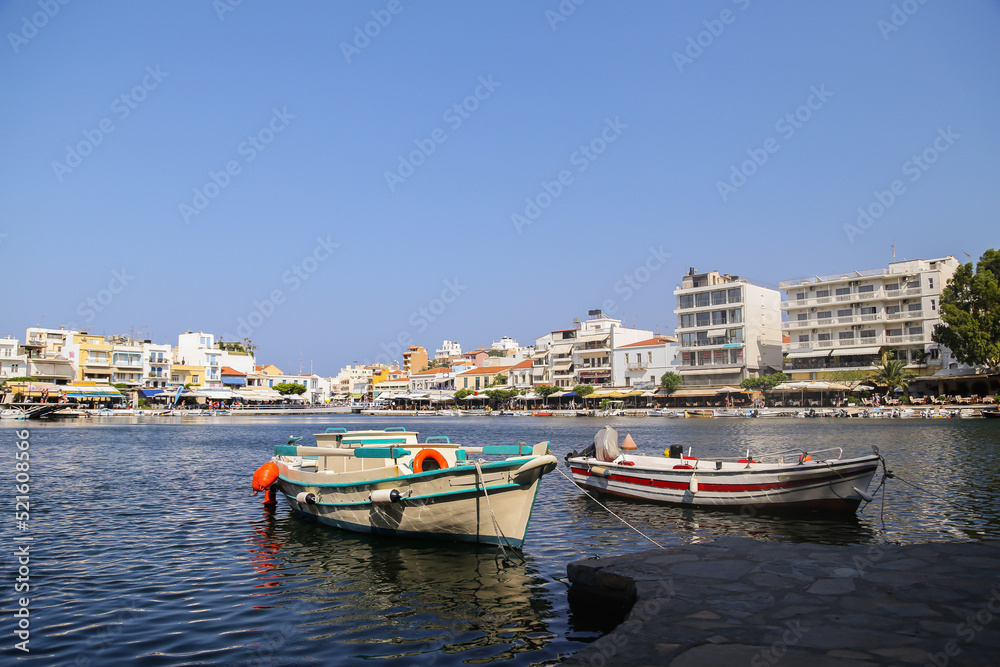 Two boats are anchored in the Greek port agios nikolaos. The area abounds with taverns and Mediterranean restaurants. Many tourists visit the port and enjoy the beautiful view.